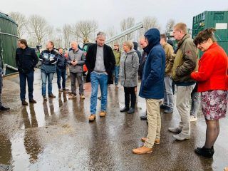 Deelnemers aan de inspiratiereis staan in de regen te kijken op het terrein van Afvalzorg Lelystad