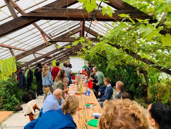 Mensen brainstormen aan lange tafel in de kas op het landgoed Roggenbotstaete.