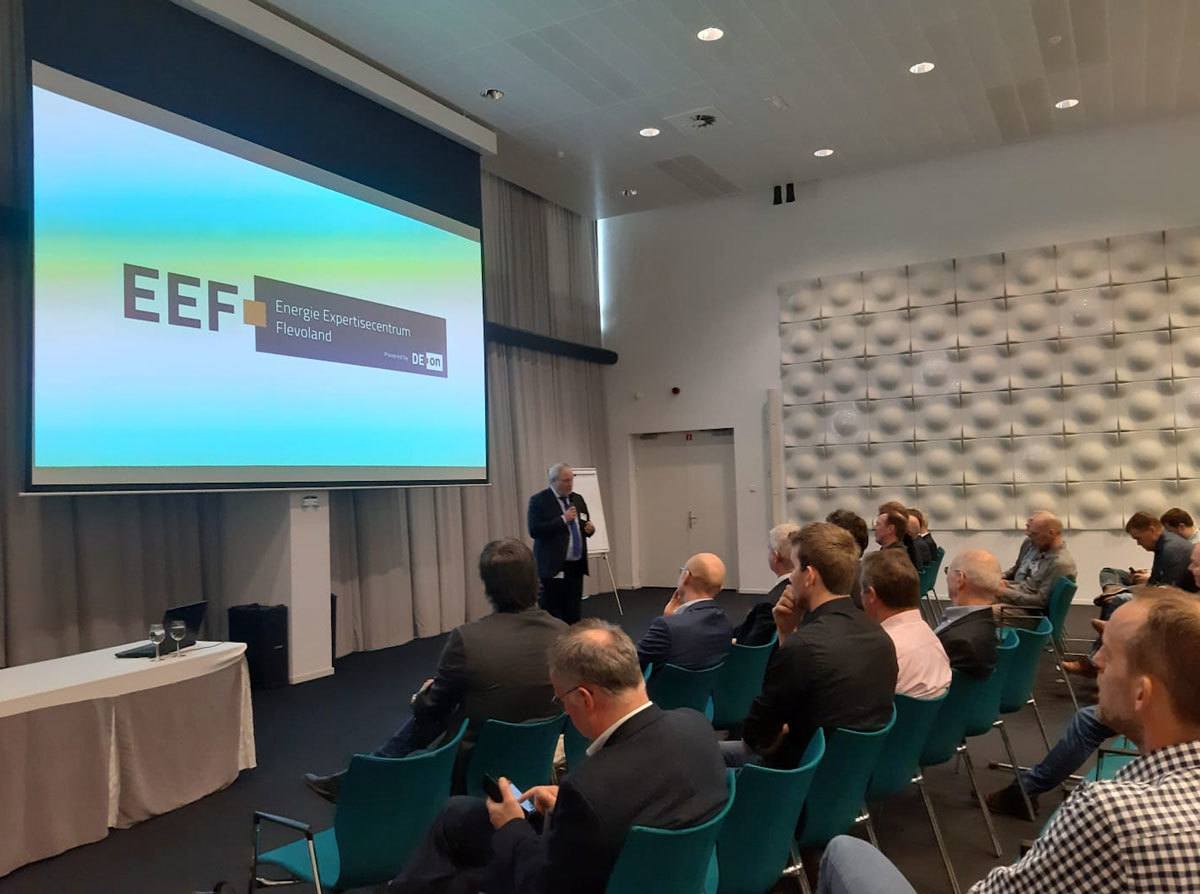 Een zaal vol mensen luistert naar de presentatie van EEF.