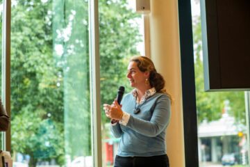 Karina Neef staat voor een groot raam en presenteert.